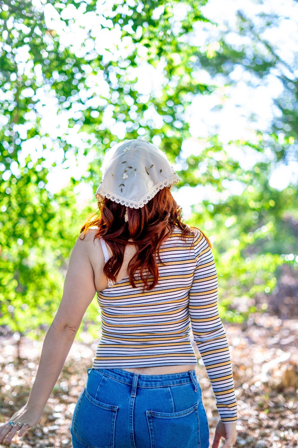 Back view wearing white cap and striped shirt in dappled sunlight through trees.