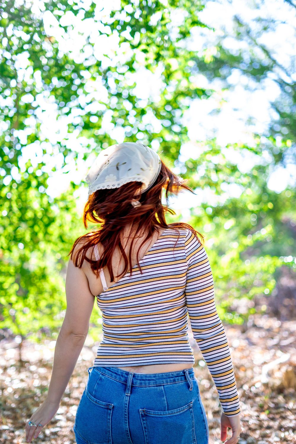 Back view of someone wearing a striped shirt and baseball cap in a sunlit wooded area.