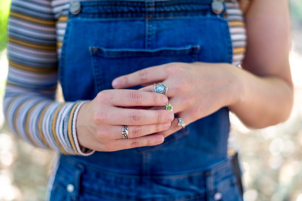 Close-up of hands wearing rings with blue denim overalls and striped sleeves visible.