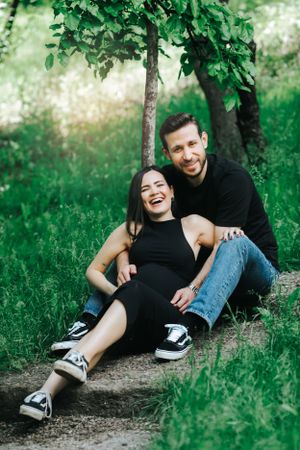 Couple sits together under green tree on sunny day.