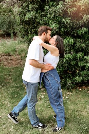 A romantic embrace between a couple in casual denim outfits standing in a garden setting with greenery.