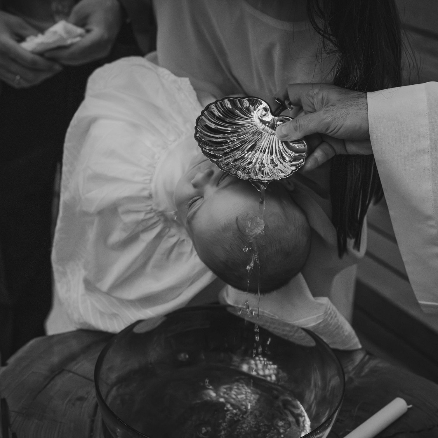Black and white photo of a infant being baptized with water poured from a shell font during a Christian ceremony.