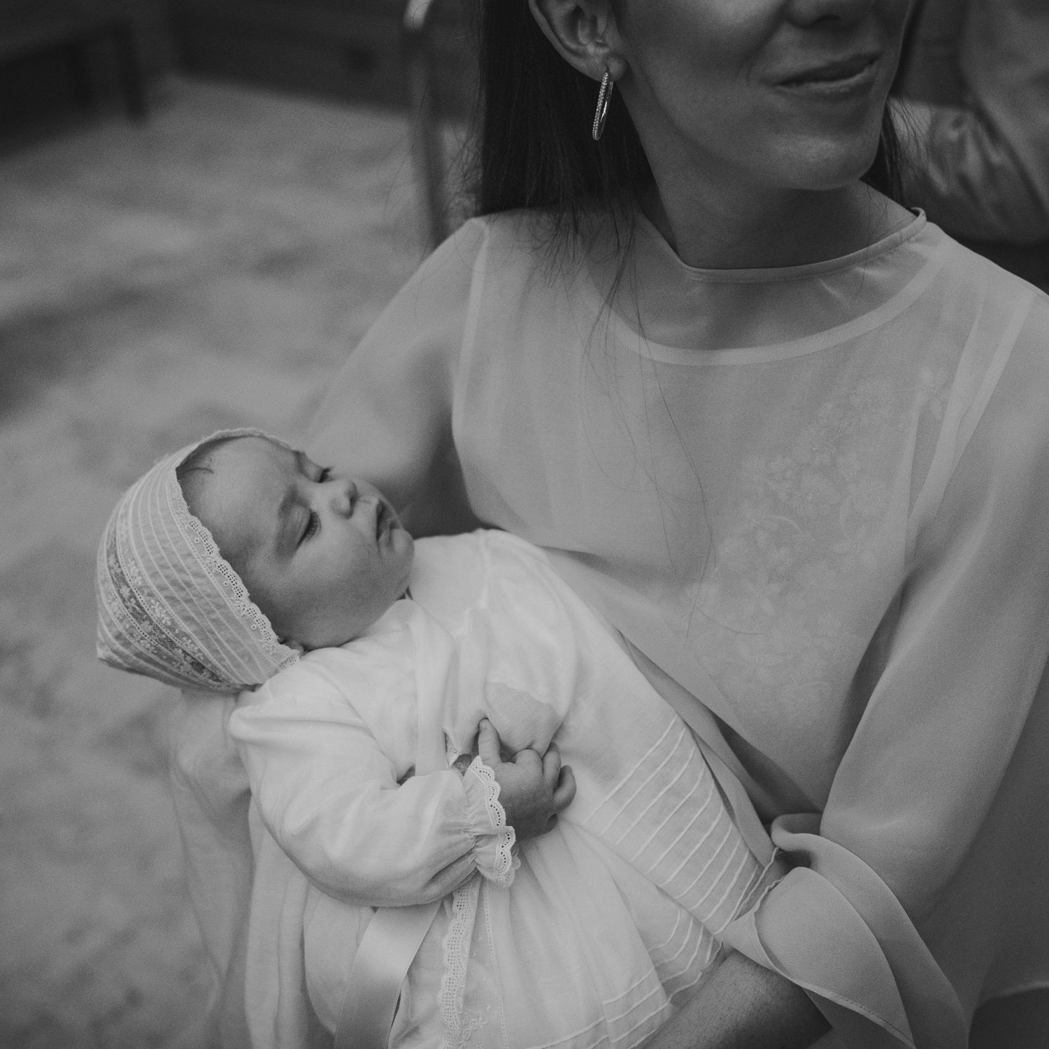 Black and white photo of a mother in white dress cradling her sleeping newborn baby wrapped in white cloth.