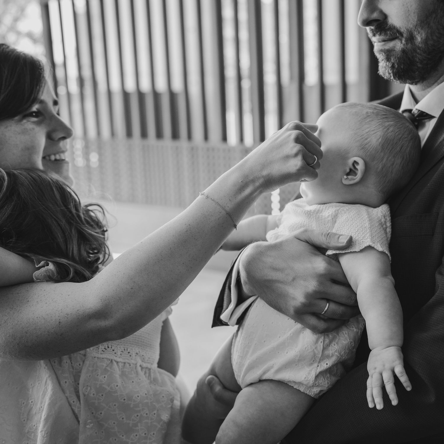 Black and white photo of a smiling bride and groom holding a newborn baby at their wedding ceremony.