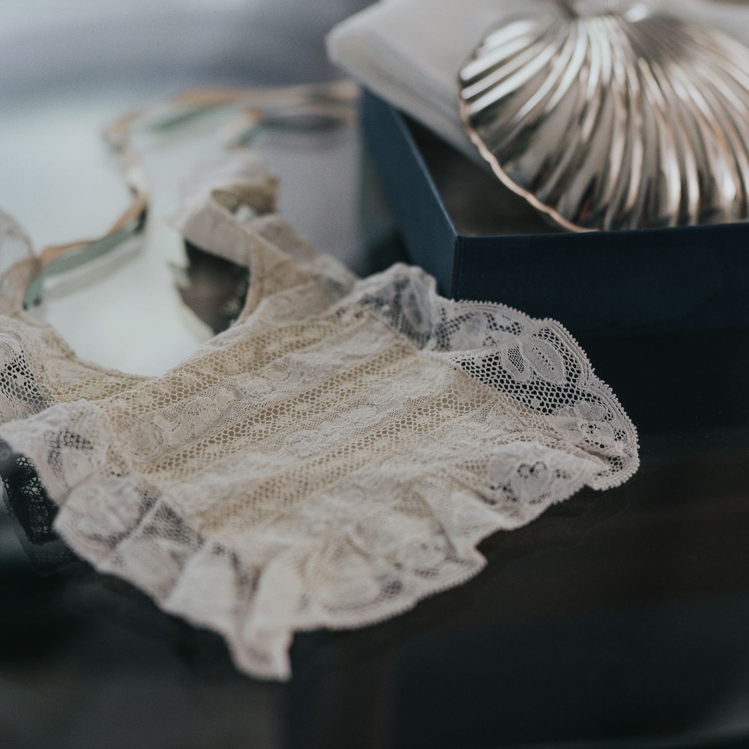 Delicate beige lace bralette displayed on a dark jewelry box with a silver decorative lid.