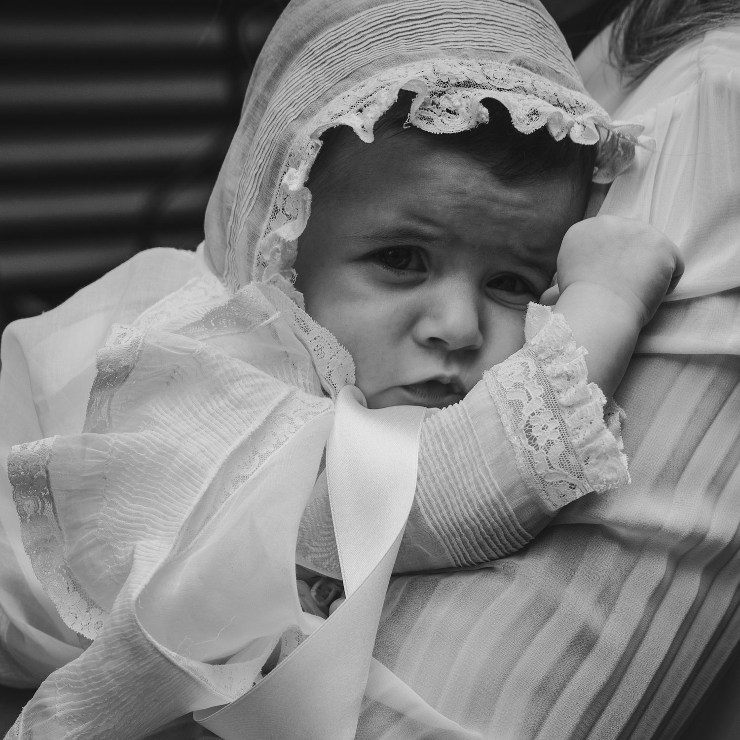 Black and white photo of a baby in a white christening gown and bonnet, resting on an adult's shoulder.