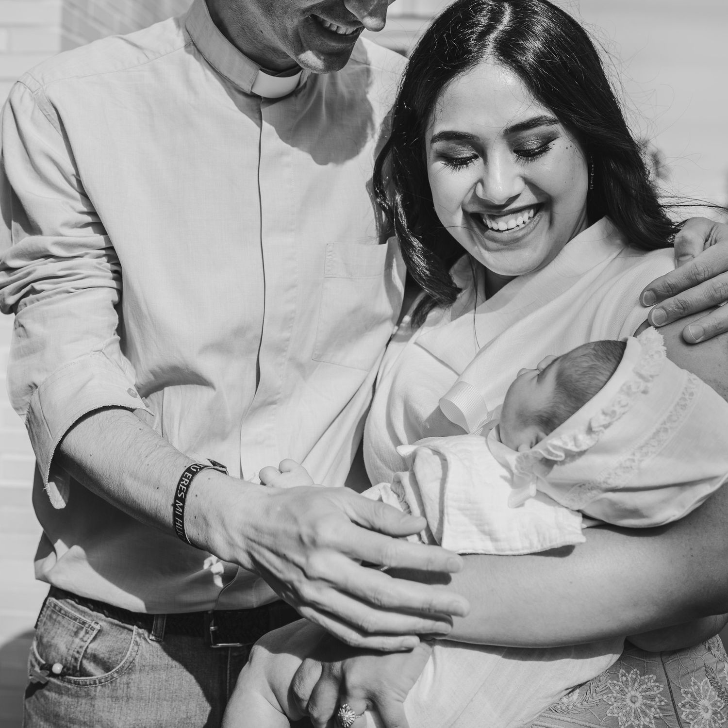 Black and white photo of smiling couple holding their newborn baby together in a bright, joyful moment.