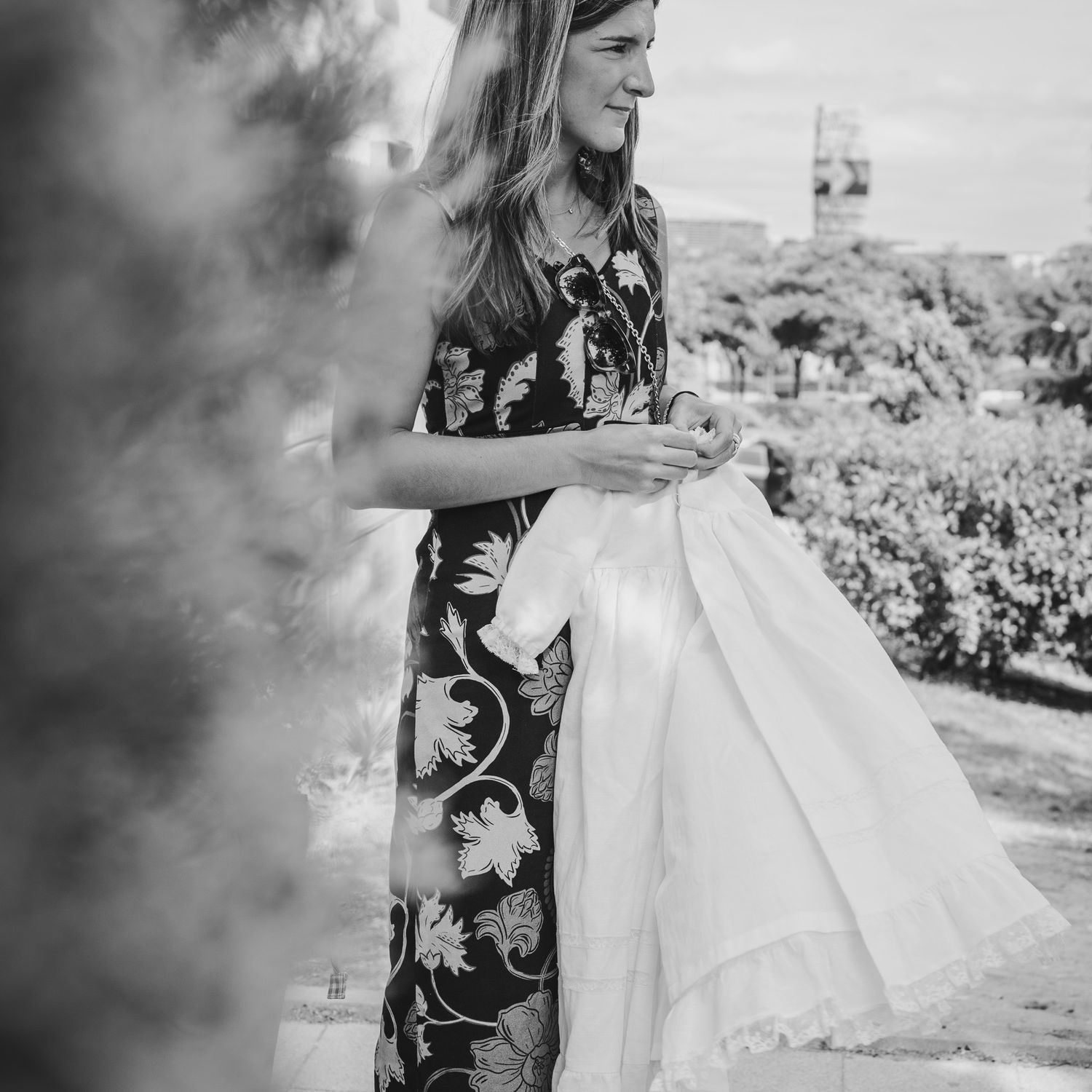 Black and white photo of a woman in a floral dress holding white fabric outdoors at a garden event.