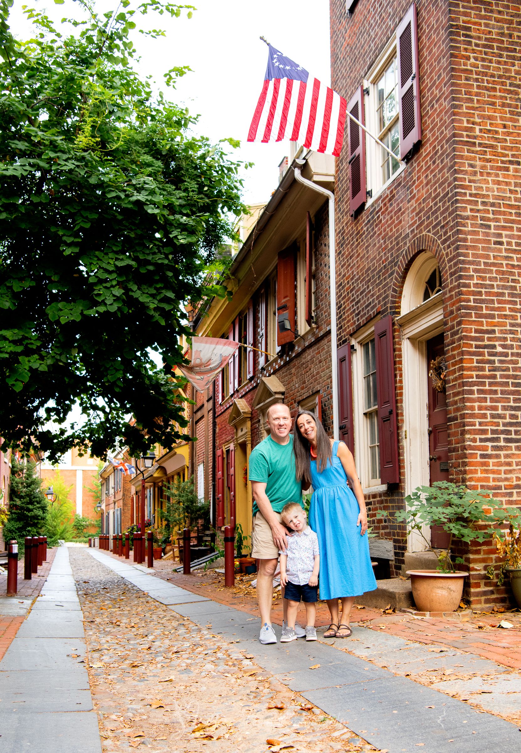 Family of three in a Philadelphia Historic brick rowhouses alley with American flags line a charming cobblestone street.