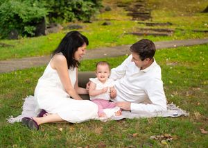 Family of three lying together on a blanket in a lush green park during an outdoor photo session.