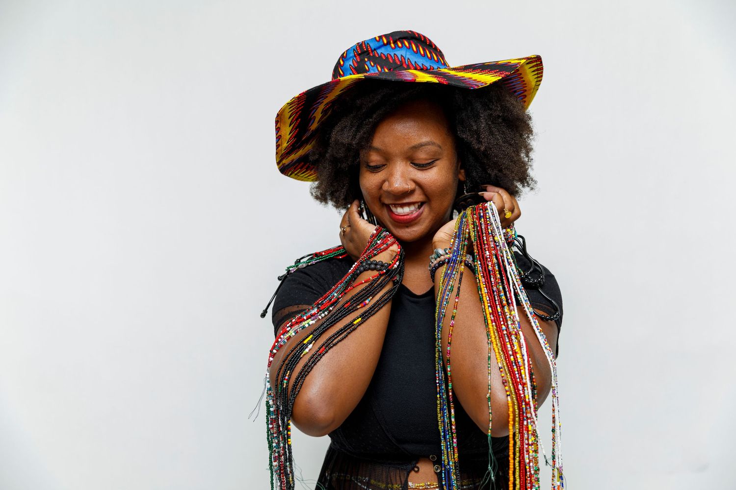 Joyful fashion portrait of someone wearing a patterned hat and black outfit against white background.