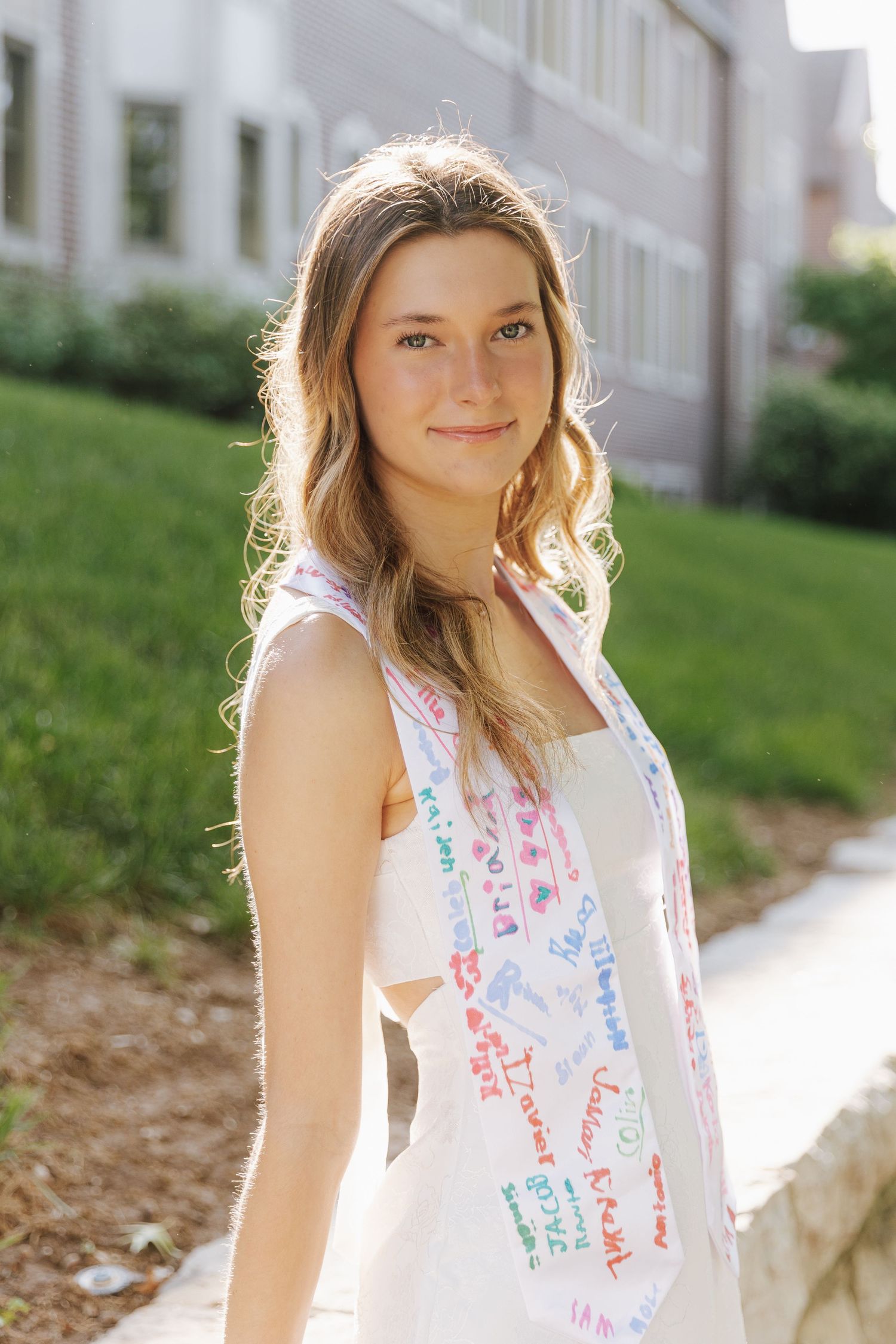 A college grad wearing a yellow stole over a blue dress, sitting while resting her head on her hand smiling softly.
