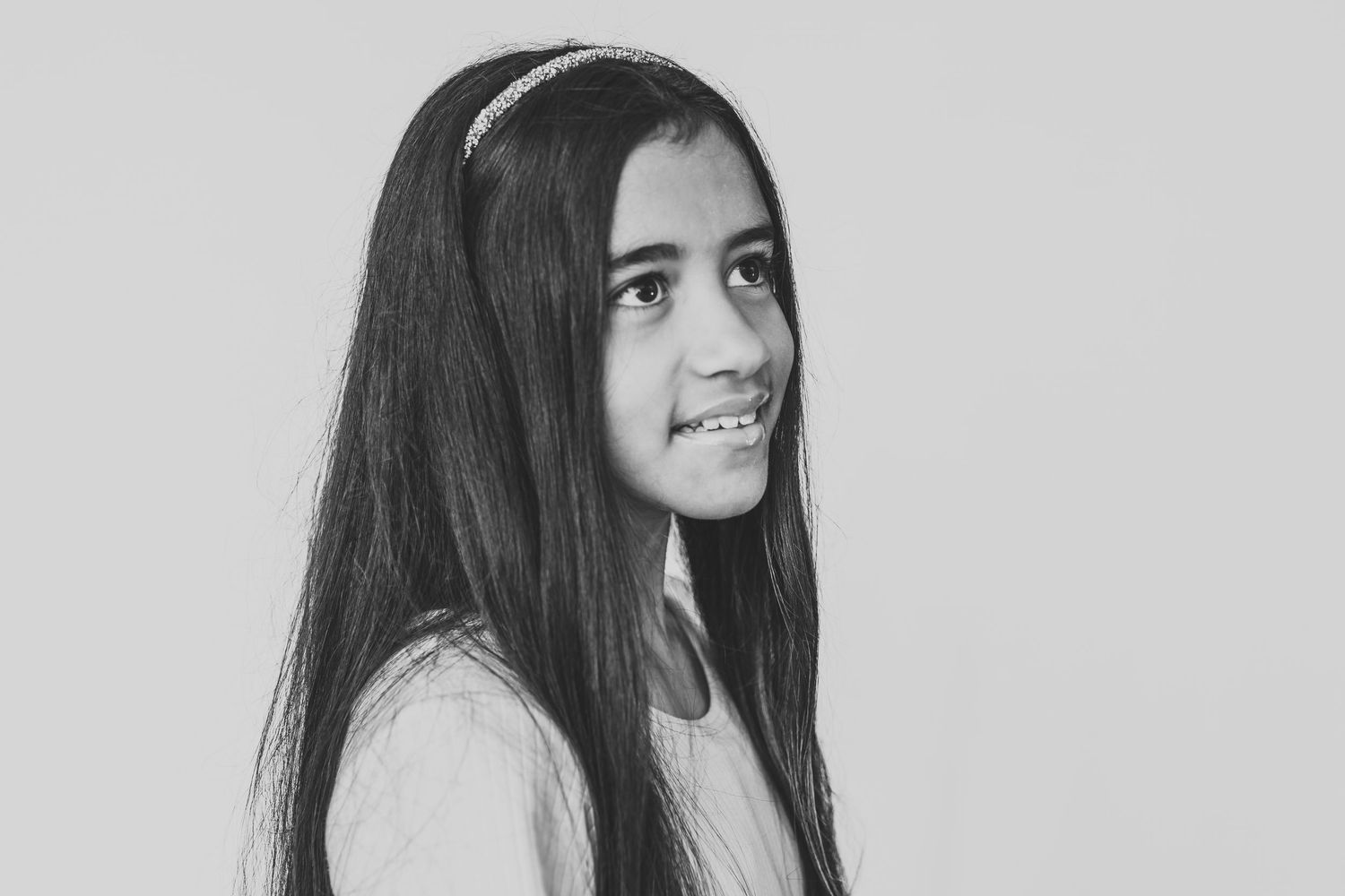 Black and white portrait of a child with curly hair in a dark sweater looking thoughtfully upward.