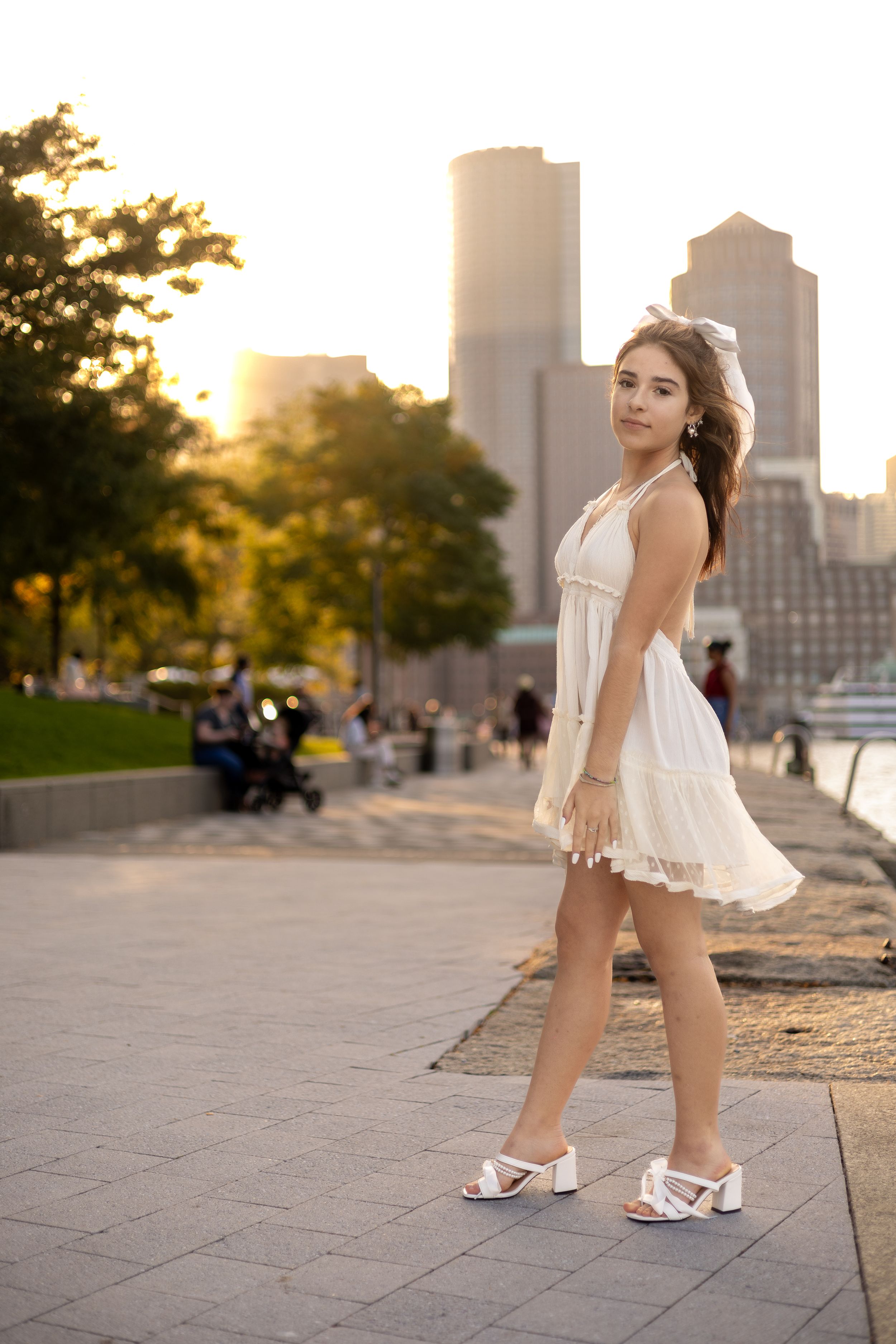 A white sundress and sandals complement the urban cityscape backdrop at sunset.