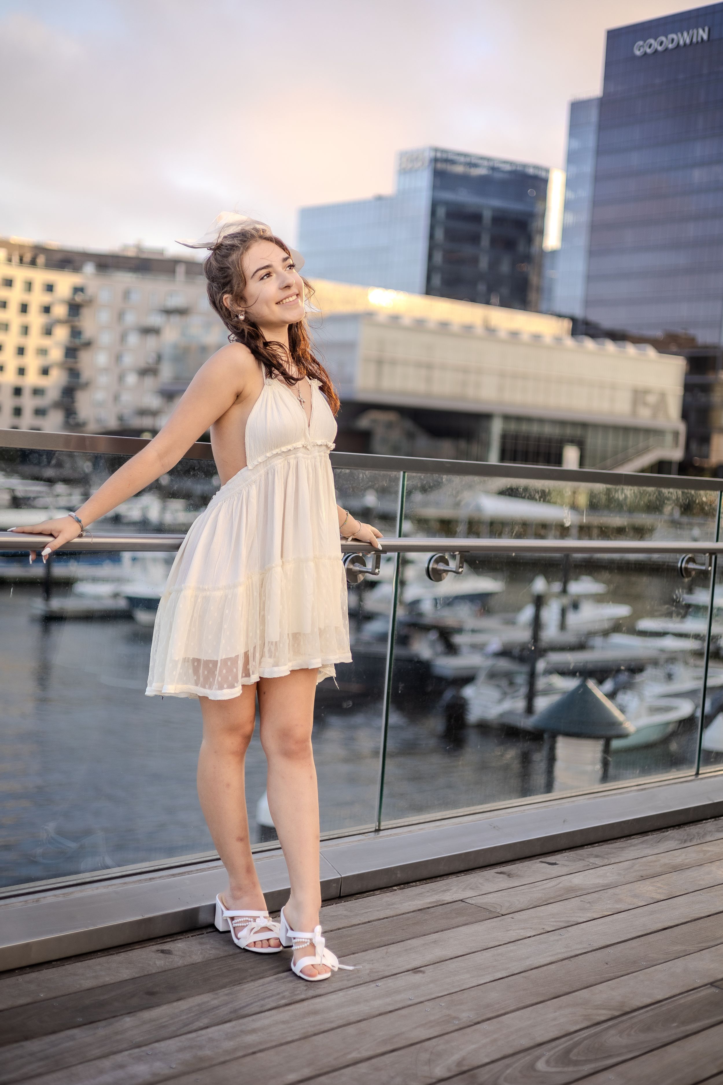 A white dress creates an elegant silhouette against a marina and city buildings at dusk.