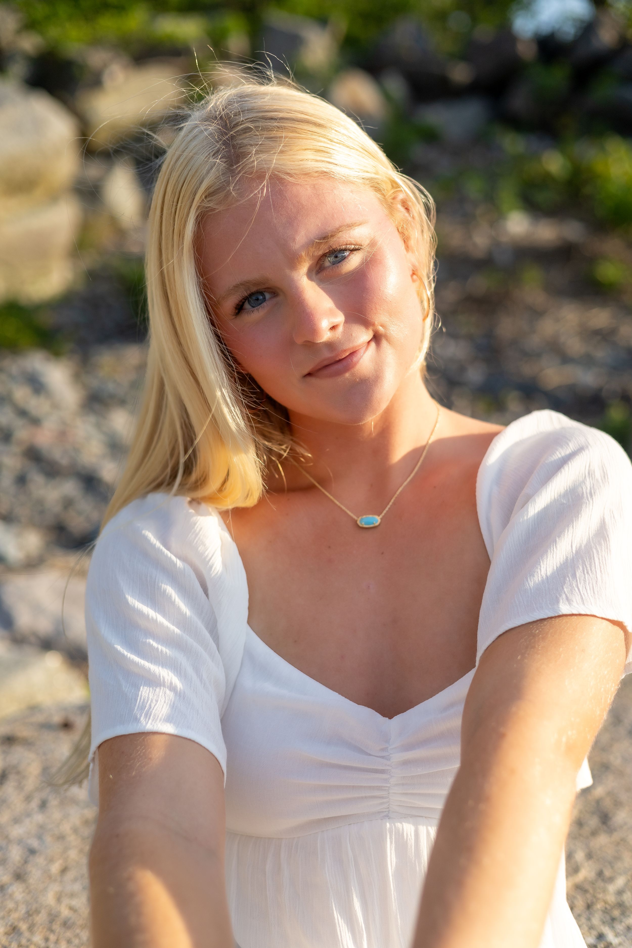 A person in a white summer dress poses outdoors during golden hour lighting.