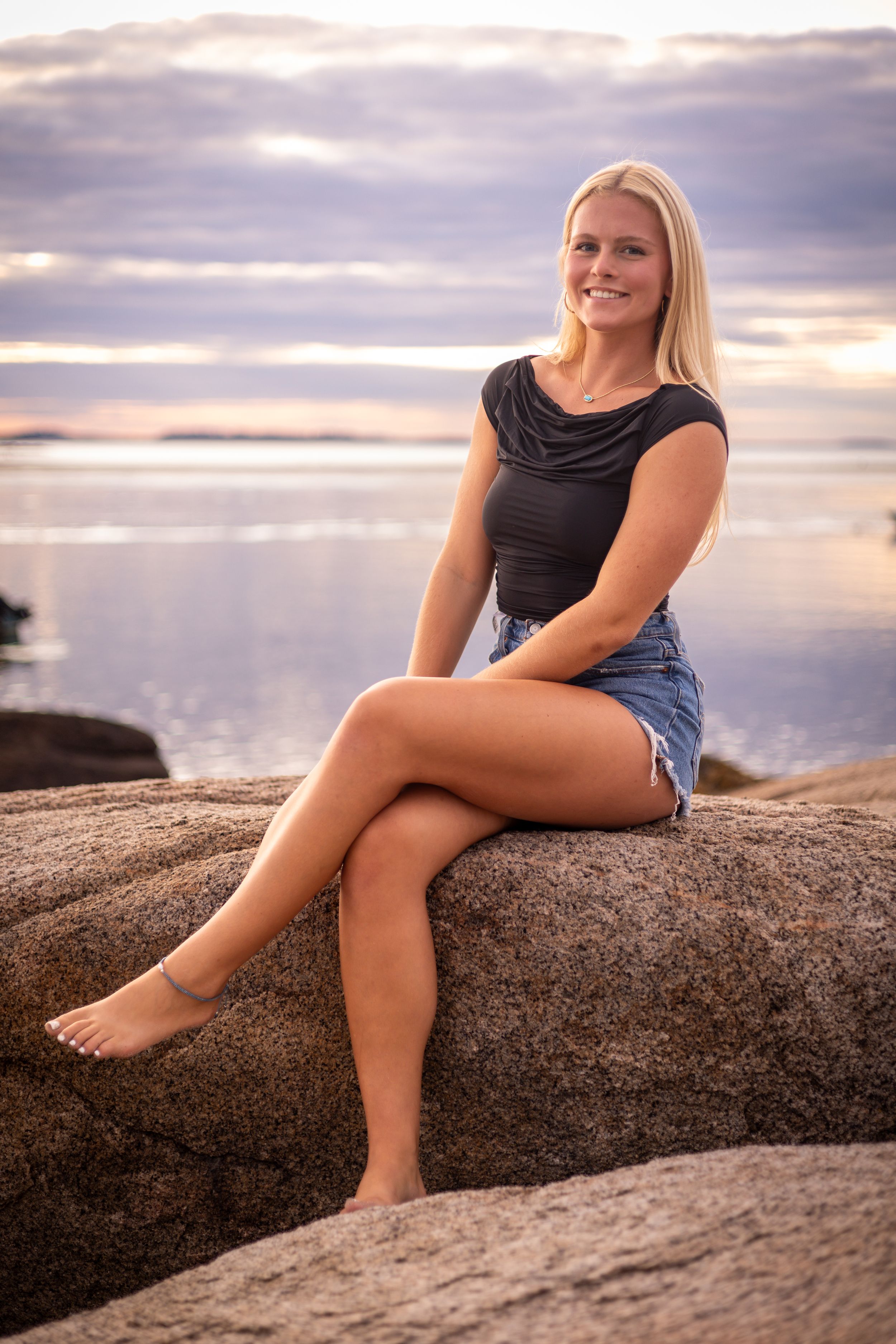 Casual beach portrait at sunset with someone sitting on coastal rocks.