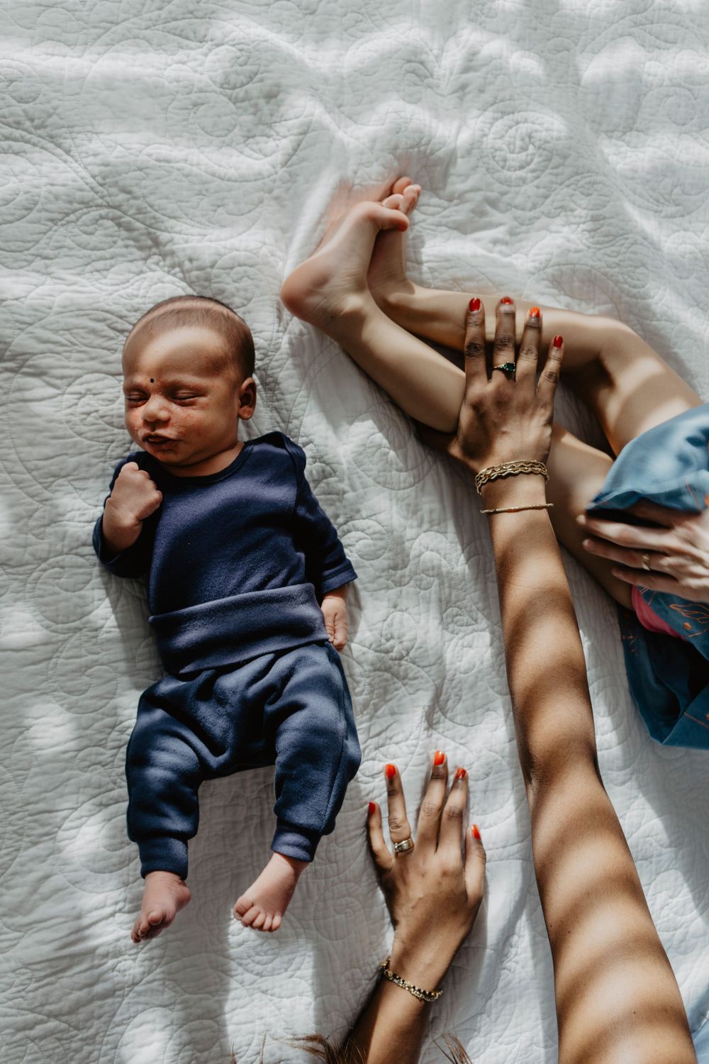Recém-nascido nos braços da irmã mais velha e da mãe, em momento íntimo de cuidado e carinho familiar no lar.
