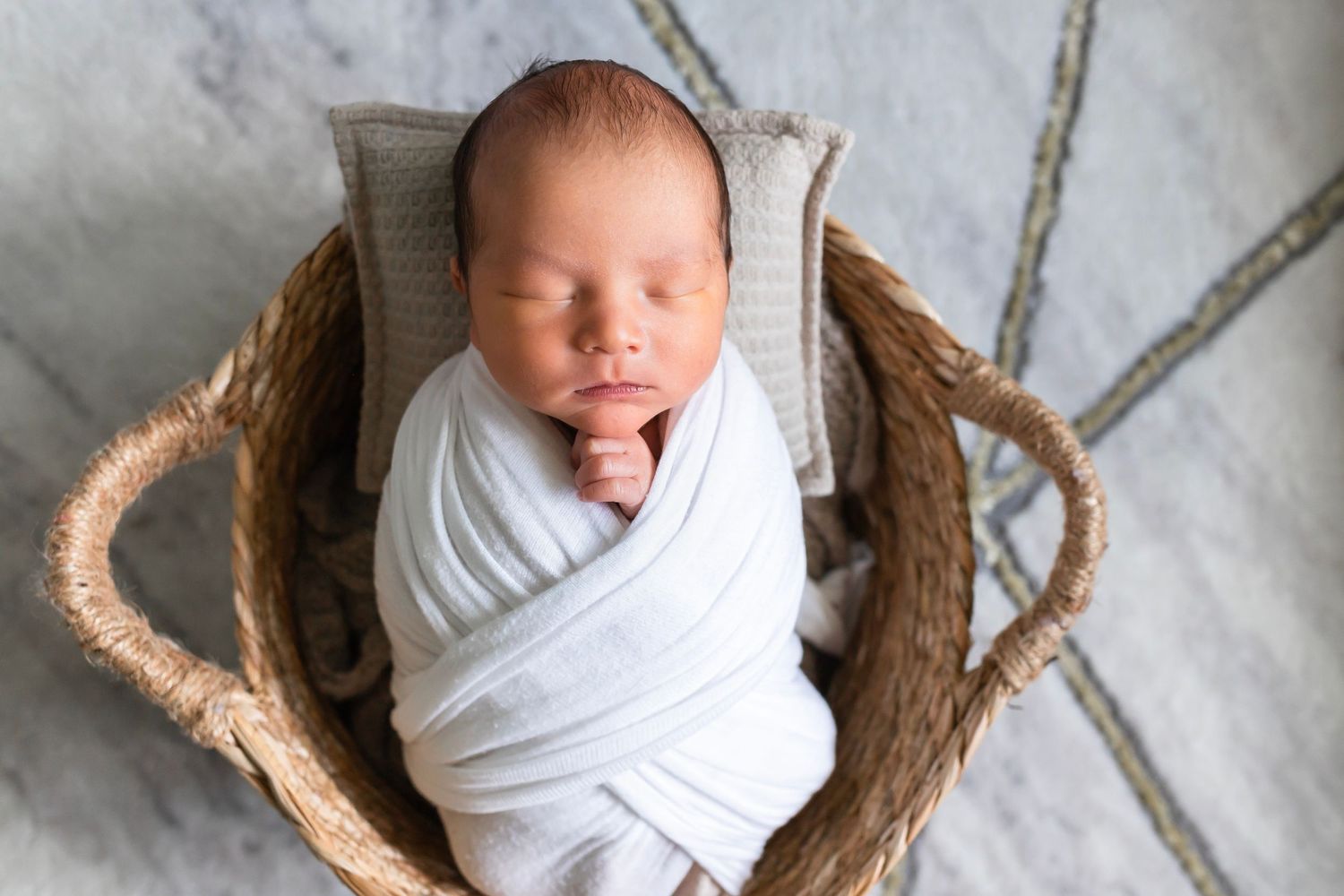 Sleeping newborn wrapped in white blanket rests in woven basket.