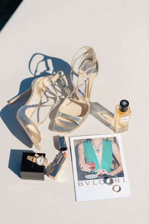 Styled flat lay of luxury accessories including silver heels, perfume bottles and a fashion magazine.
