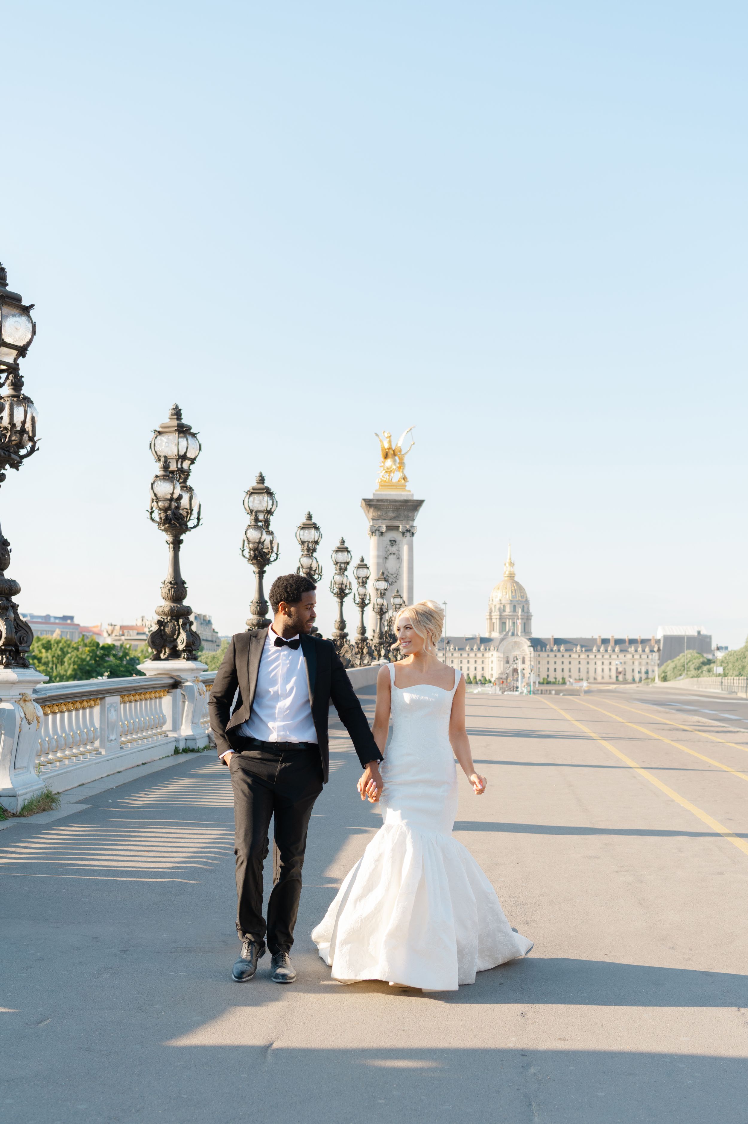A couple walks together along a scenic bridge with ornate lampposts and stone railings in Paris.
