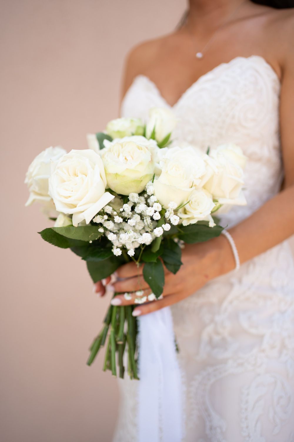 Bridal bouquet of white roses and baby's breath held against lace wedding dress.