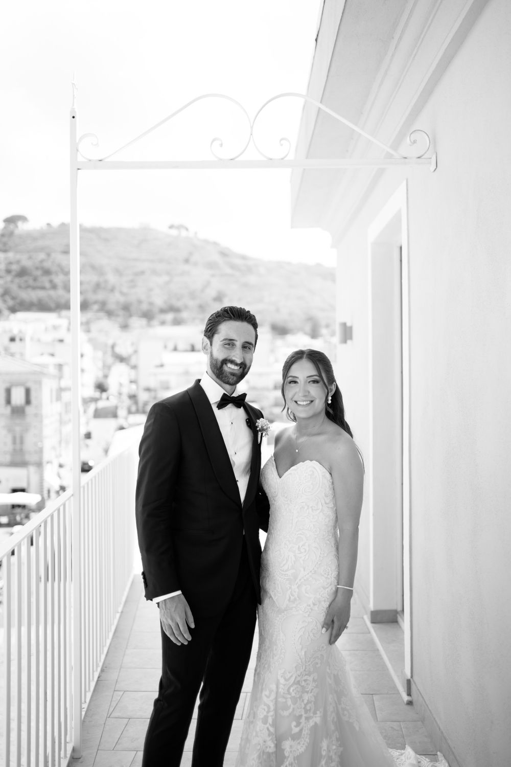 Wedding couple shares intimate moments on a bright white balcony overlooking a coastal landscape.
