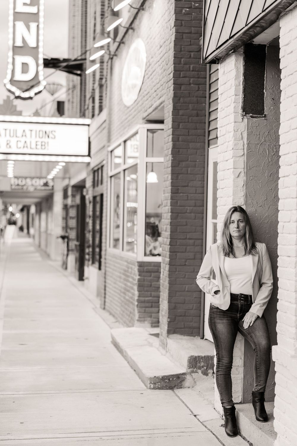 A black and white image of a women leaned up against a brick building surrounded by theater light with a calm expression