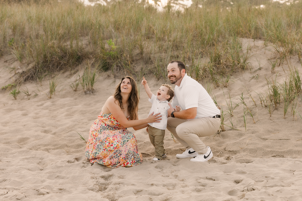 A family plays together on a sandy beach dune during a sunset photo session.