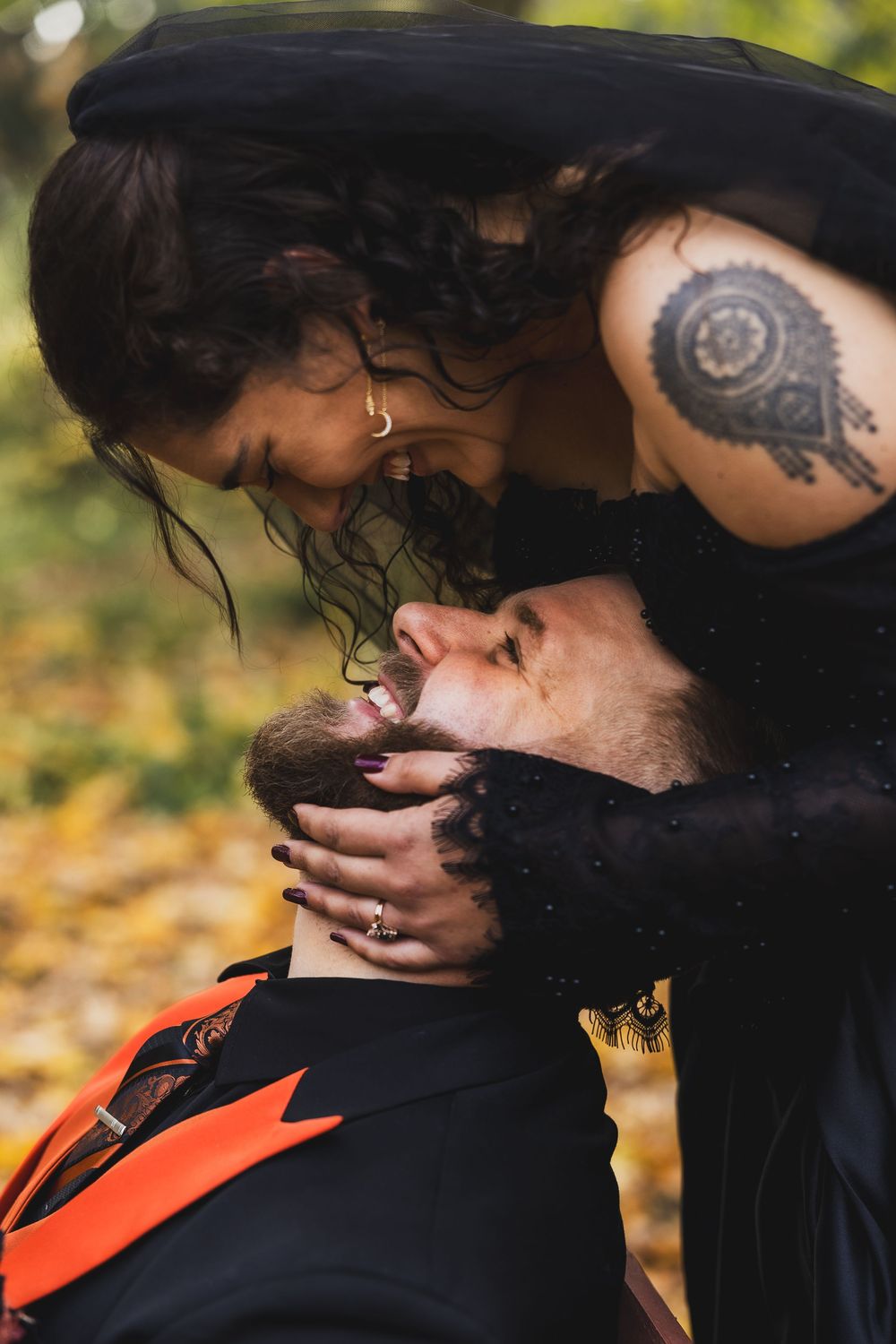 A bride wearing a black dress cupping the cheeks of her new husband below her.
