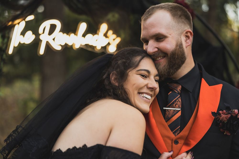 A couple in orange and black attire shares a joyful moment during a wedding at an outdoor photo session.