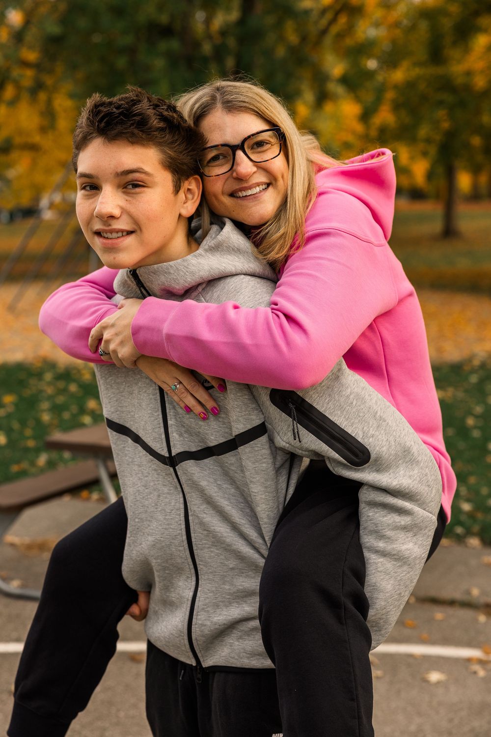 A couple embraces and smiles together in an autumn park setting with fallen leaves and warm lighting.