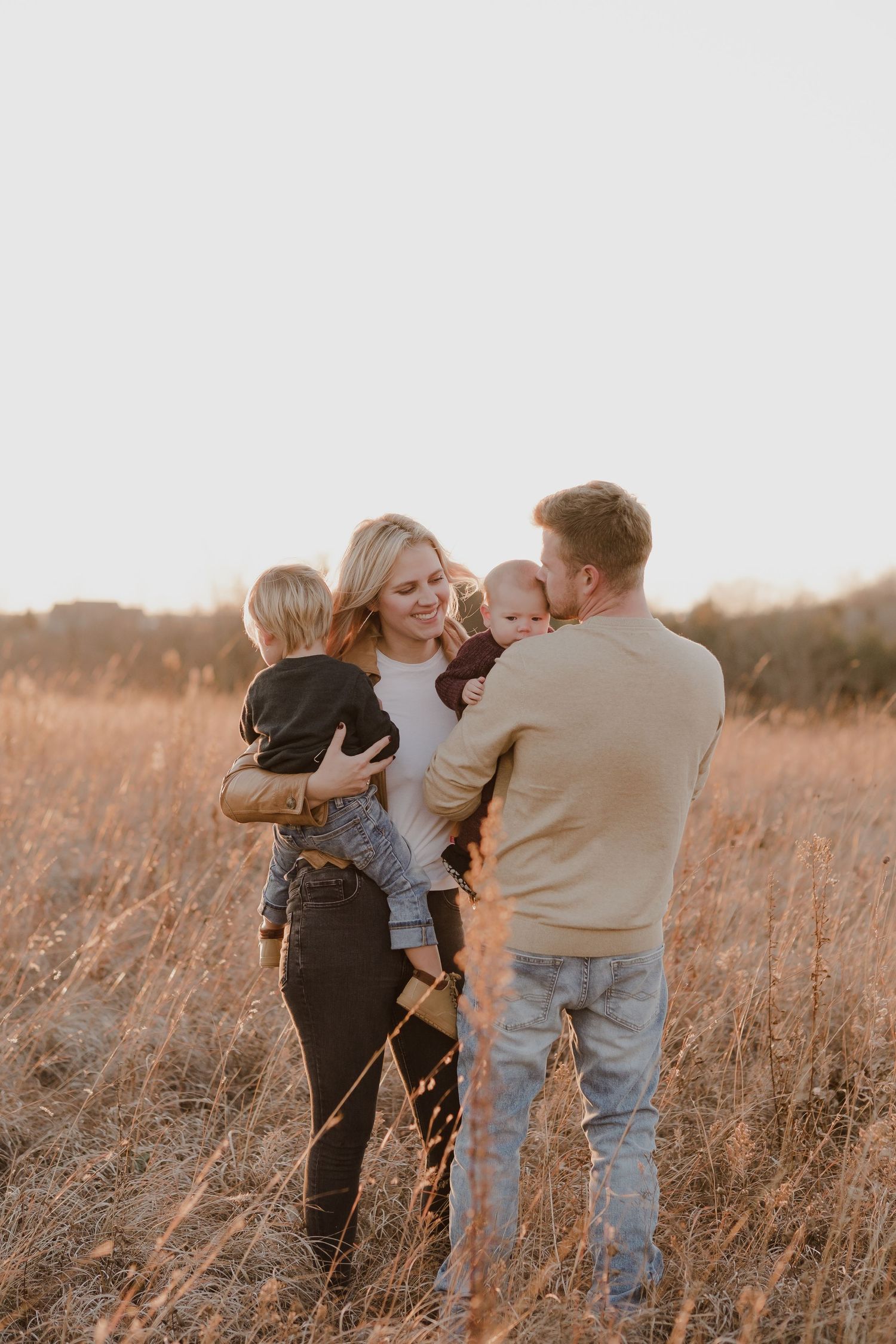 Group embracing and laughing together in a golden field during sunset.