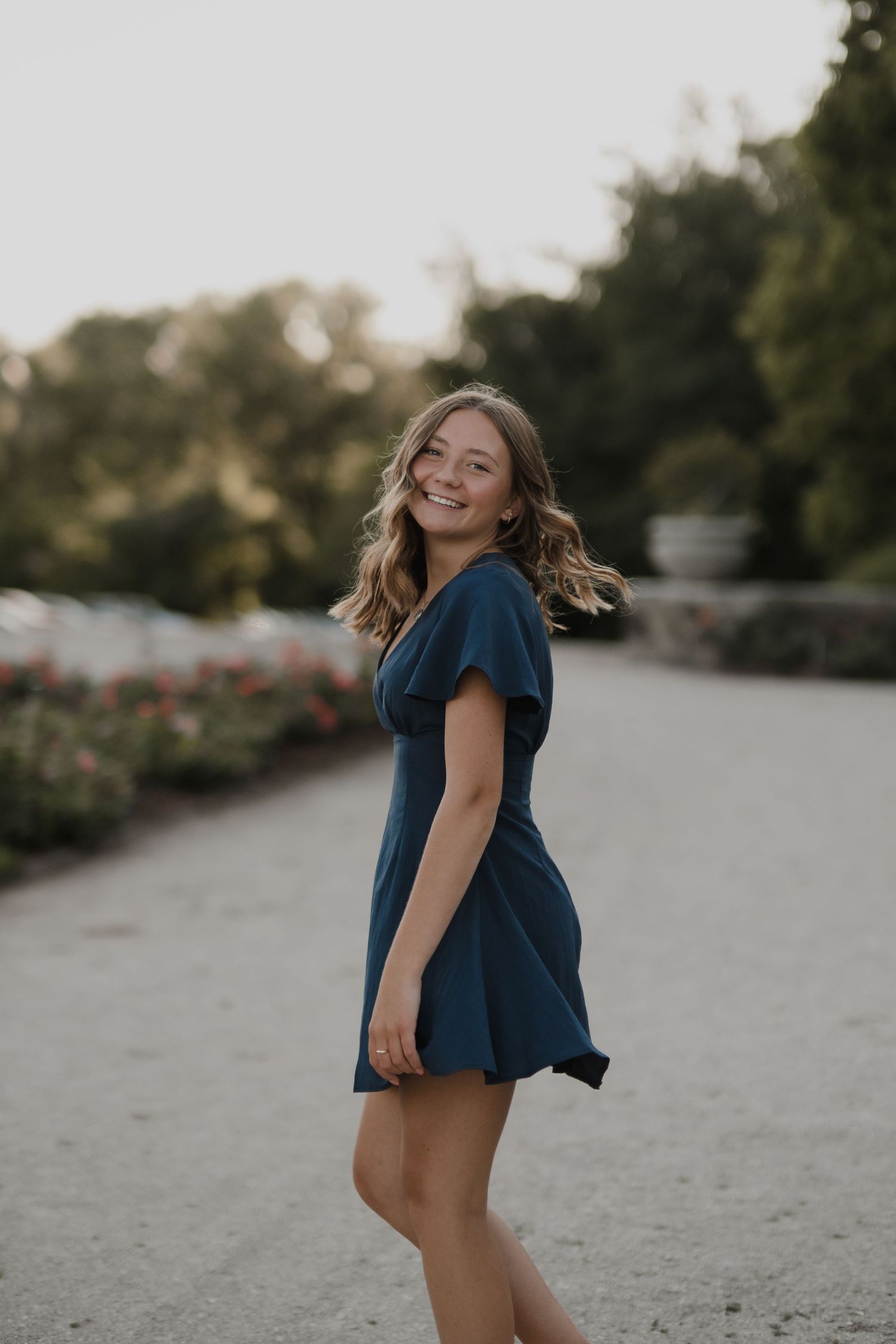 Person in navy dress twirling playfully in outdoor setting at sunset.