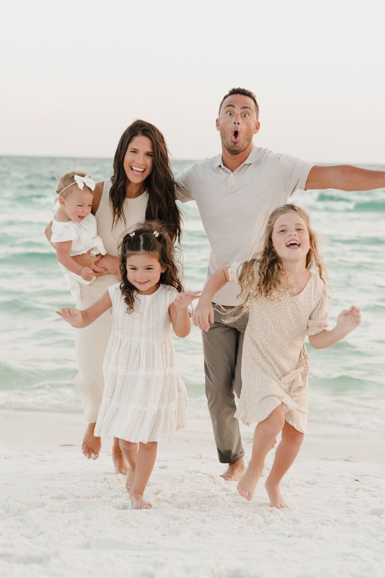 Family plays together on white sandy beach by ocean waves.