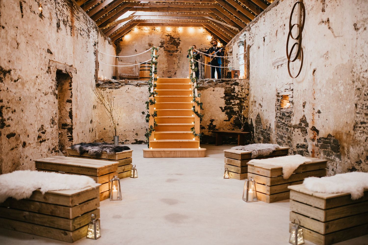 Rustic stone cellar with wooden staircase and benches decorated with string lights.