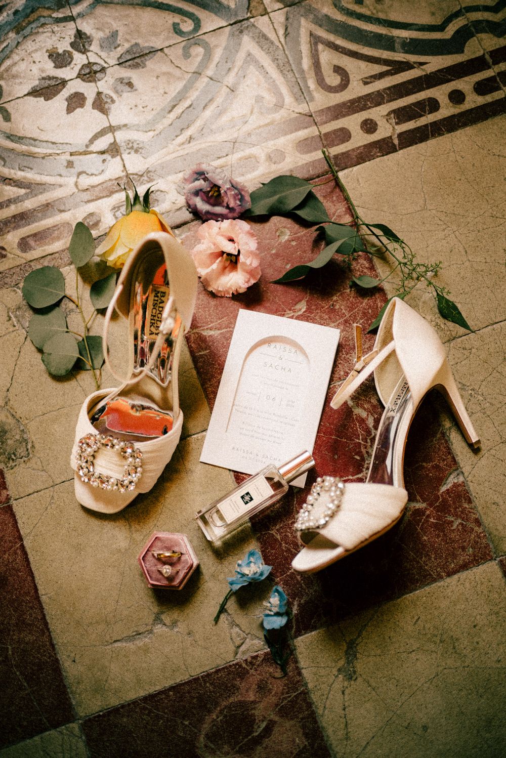 Wedding accessories including bridal shoes, flowers and invitation details arranged on a decorative floor.