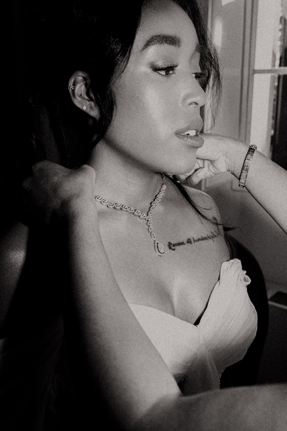 Black and white portrait of someone wearing a delicate necklace in dramatic lighting.