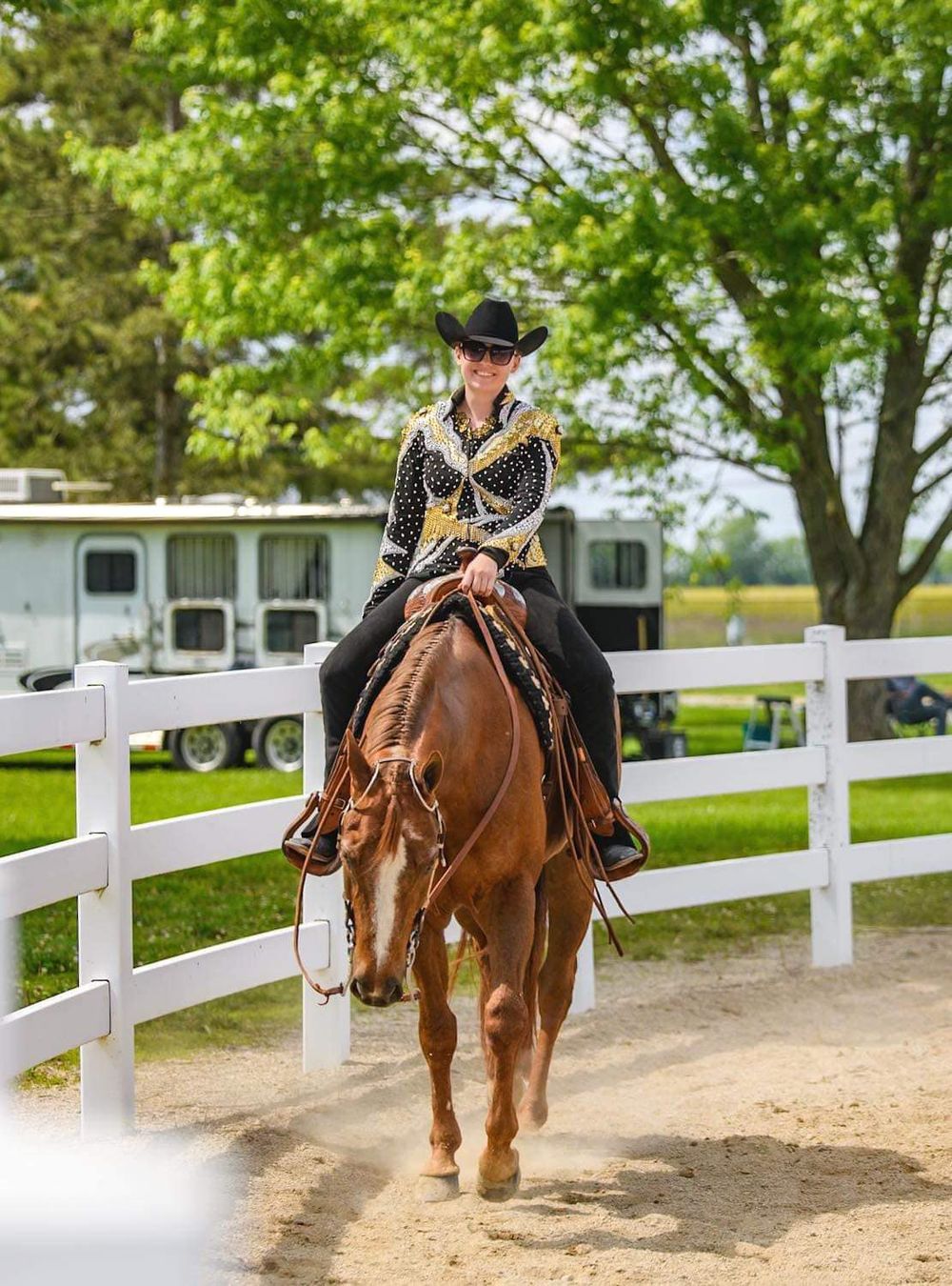 Equestrian rider in traditional attire guiding horse through arena with white fence.