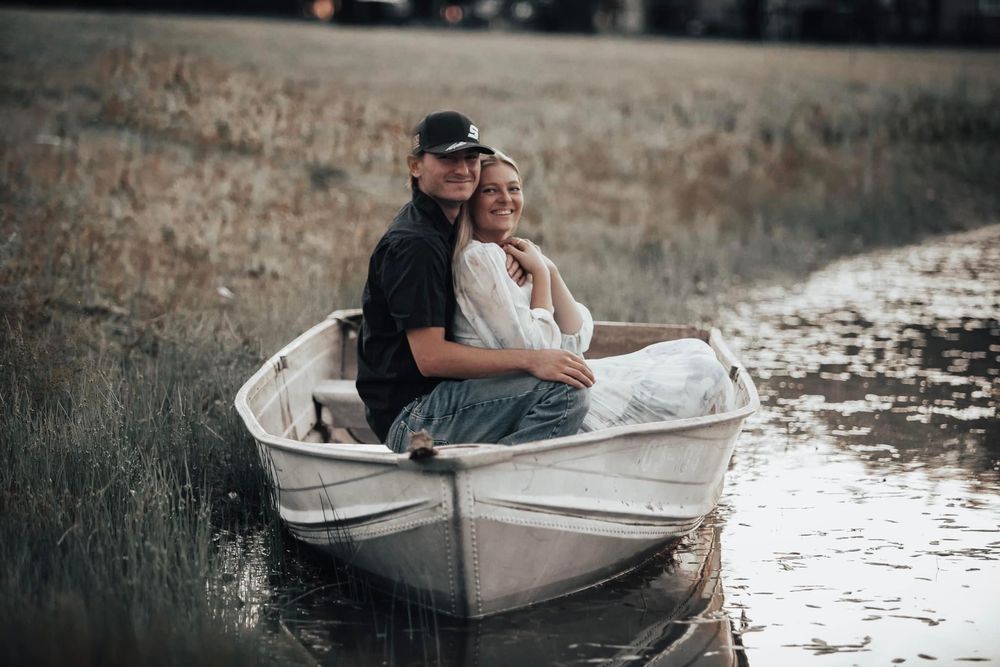 Couple sitting together in small white boat on calm waters at sunset.