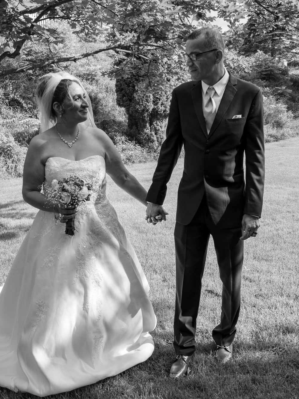 Black and white wedding photo of couple sharing tender moment in garden setting.