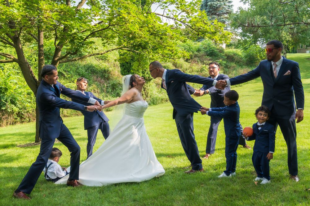 Playful wedding party photo with fun action poses on green lawn.