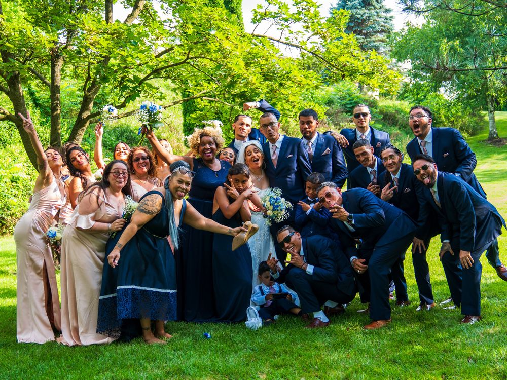 Large wedding party group photo with fun poses in lush garden setting.