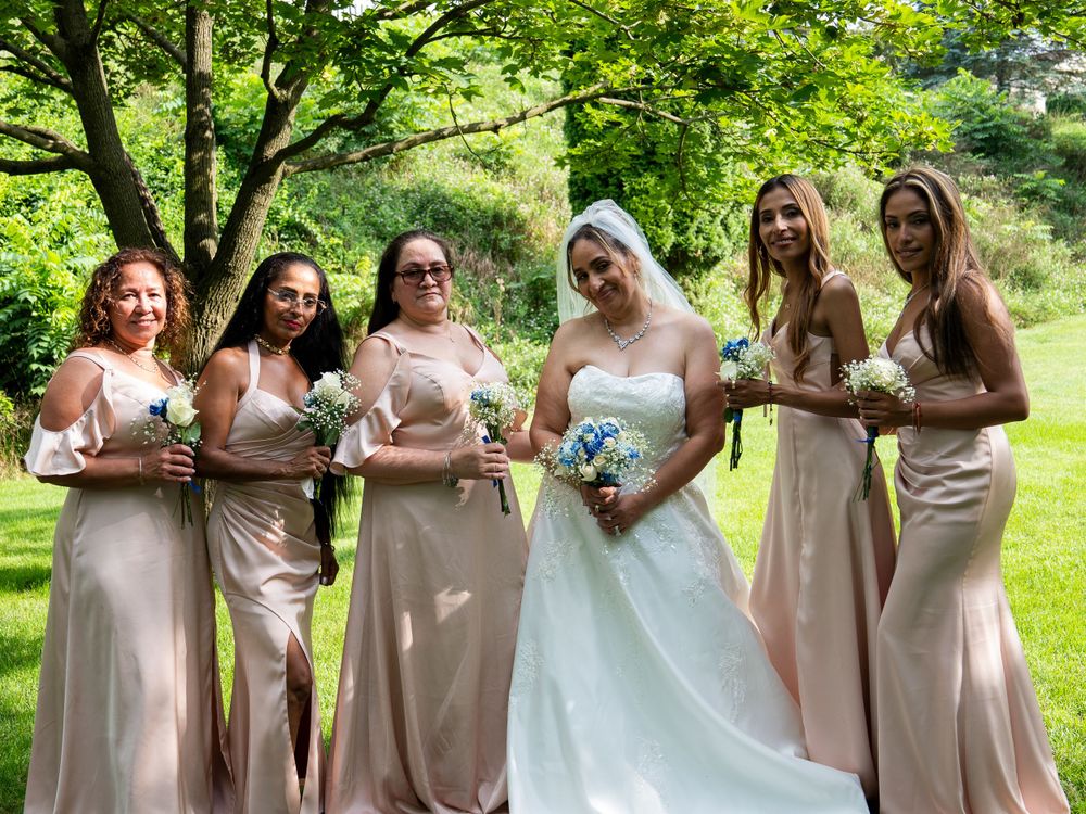 Bridal party in blush pink dresses posing with bride in white gown outdoors.