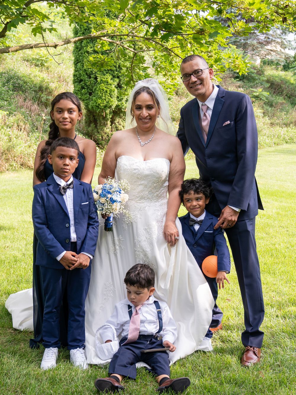 Family portrait at a wedding with children in formal attire standing on a grassy hill.
