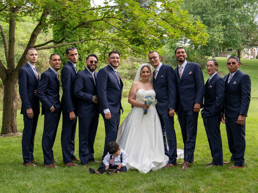 Wedding party in navy suits and white gown pose together on a lush green lawn.