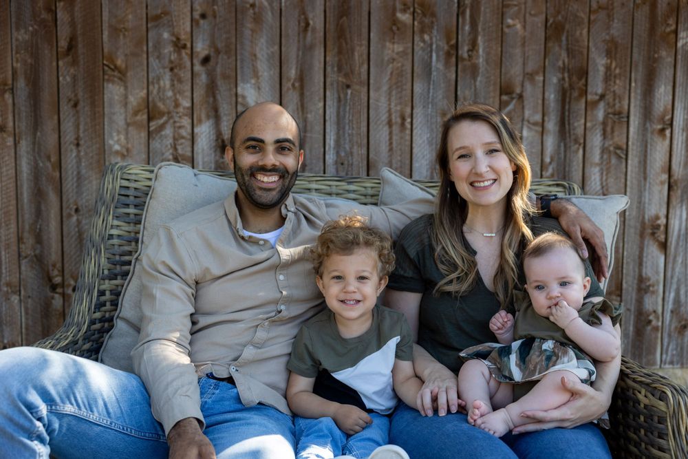Family of four sitting together outdoors against rustic wooden fence background.