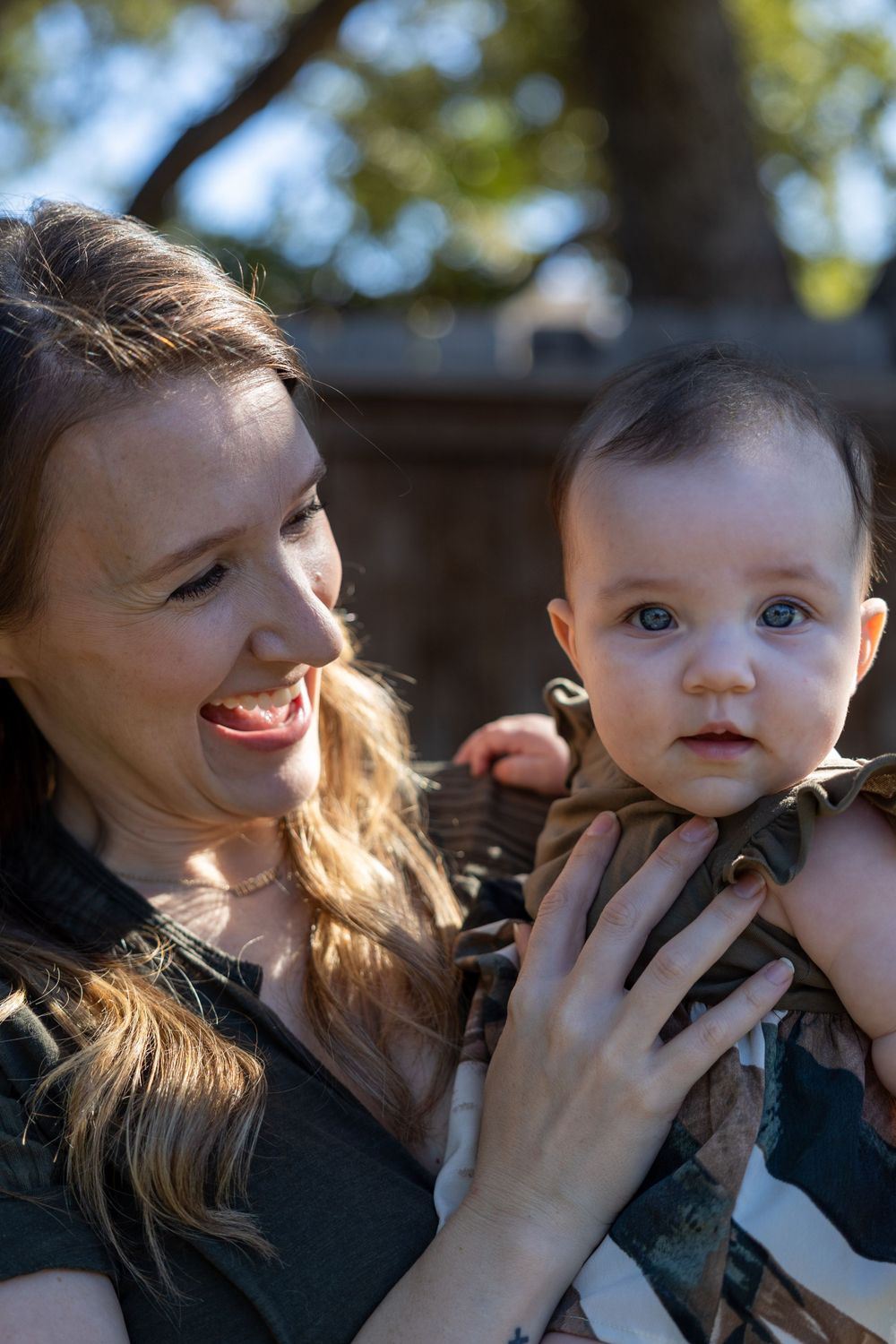 Candid outdoor portrait of parent and baby sharing a happy moment in natural lighting.