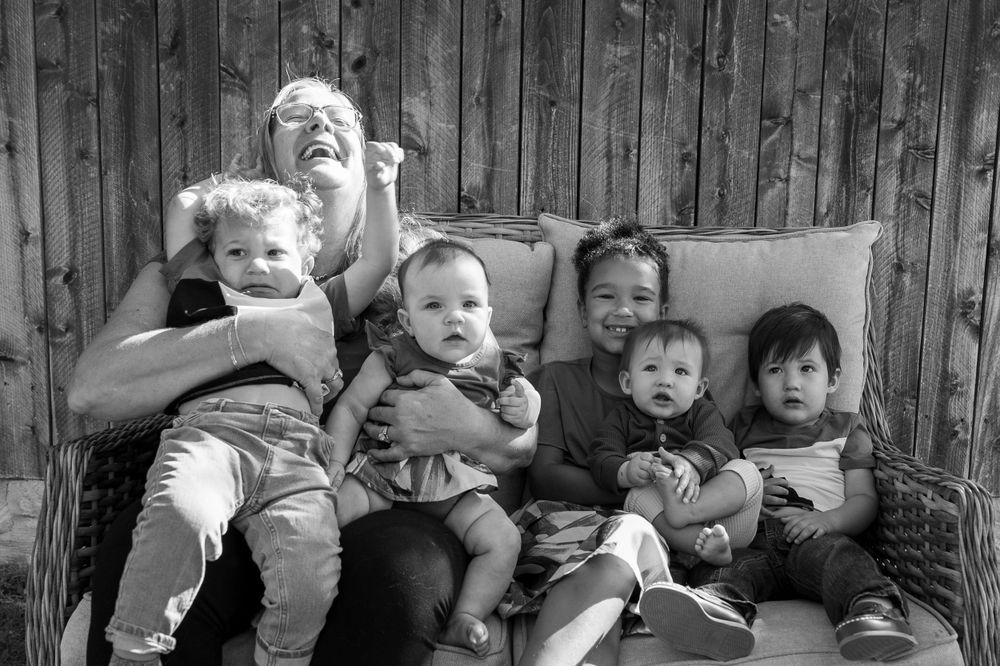 Black and white portrait of children and adult sitting together on outdoor furniture.