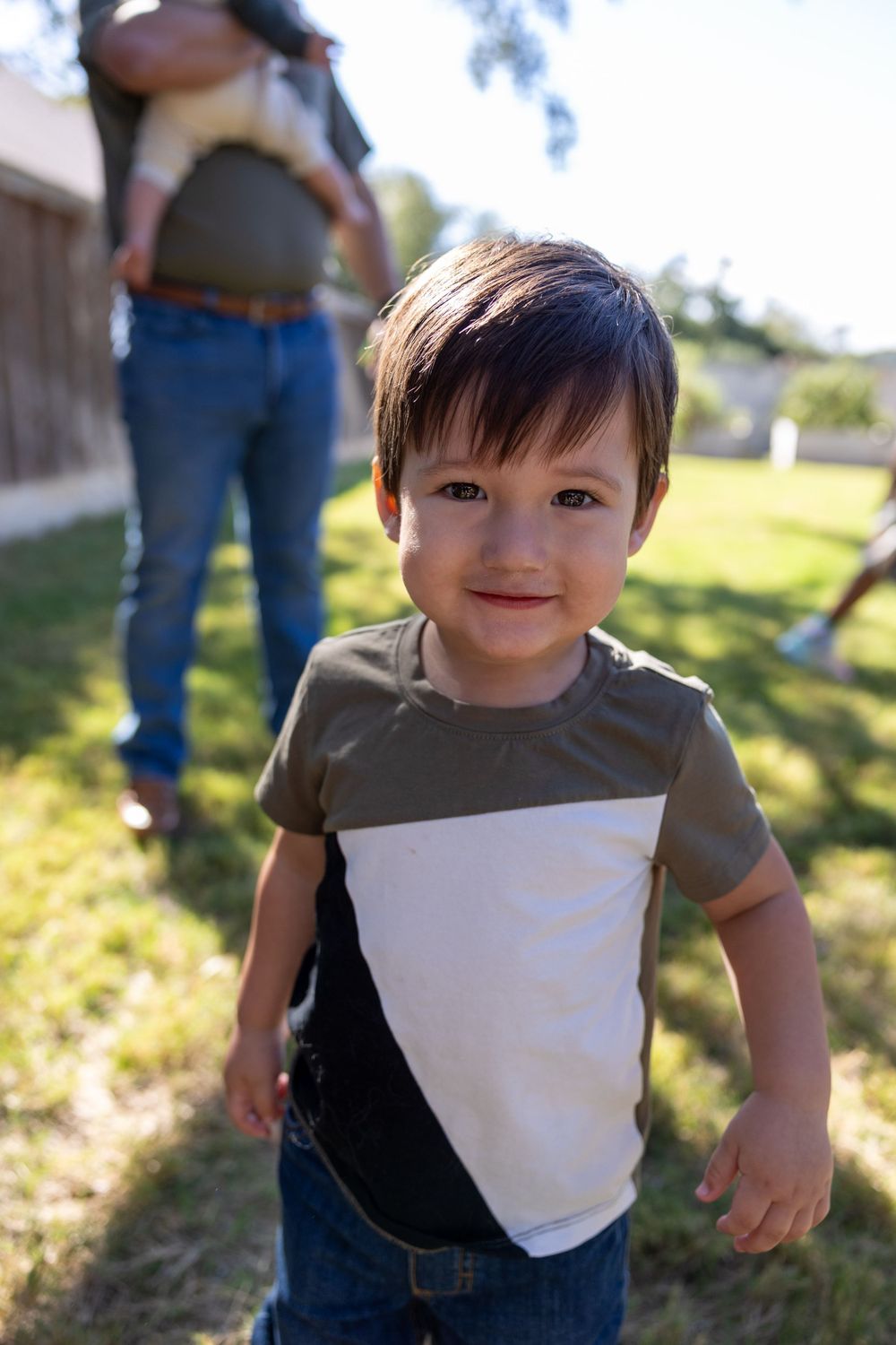 Young child in striped t-shirt smiling outdoors in backyard setting for family portrait session.